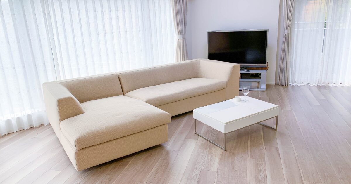 白いカーテンとL字ソファがあるシンプルなリビングルーム